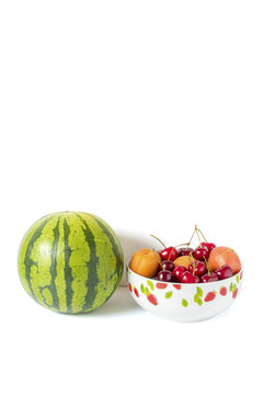 Eine Melone und eine Obstschale mit Kirschen und Pfirsiche mit Kirschen und Pfirsiche vor einem weißen Hintergrund