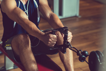 Close-up shot of young muscular man doing exercise on rowing machine at modern gym while having...