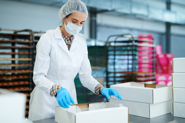 Confectioner in white coat preparing empty paper box at factory. 