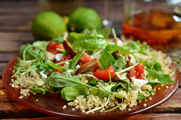 Arugula salad with quinoa and mushrooms on a red plate on a wooden background