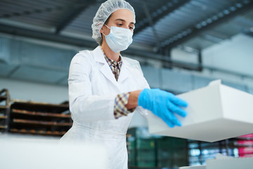 Confectionery factory employee standing in white coat and holding paper package box.