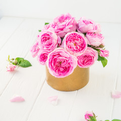 Close up tender pink tea roses bouquet in vintage golden pot on the white wooden table. Floral background. Postcard mock up. Summer, spring flowers. Square card. Selective focus. Copy space.