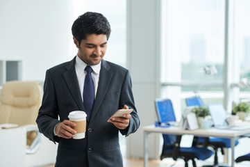 Indian businessman drinking coffee and using his mobile phone at office