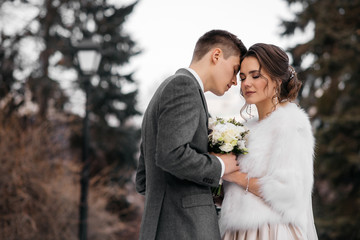 Loving and beautiful bride and groom stand in an embrace in the winter forest
