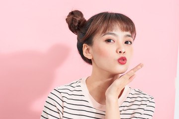 Slender asian woman with bun hairstyle tenderly touching cheek with palm and smiling cheerfully at camera while standing over pink wall.