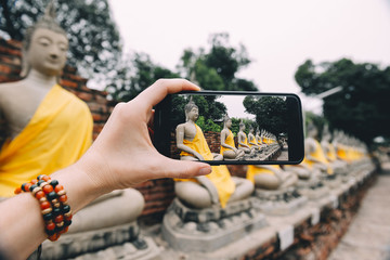 Hand taking photo of Buddha statues with smartphone