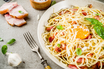 Traditional italian pasta, spaghetti carbonara with bacon, creamy sauce, parmesan cheese, egg yolk and fresh basil leaves grey stone background copy space