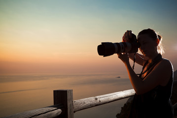 Young woman photographer shooting sunset by the sea