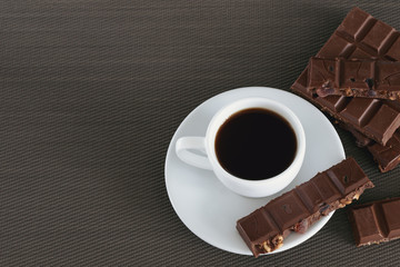 White cup with black coffee and chocolate on a brown background