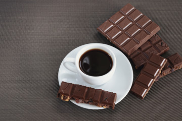 White cup with black coffee and chocolate on a brown background