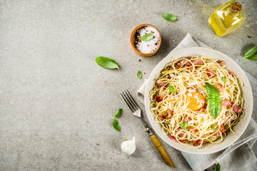 Traditional italian pasta, spaghetti carbonara with bacon, creamy sauce, parmesan cheese, egg yolk and fresh basil leaves grey stone background copy space
