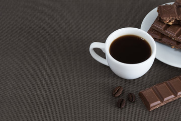 White cup with black coffee and chocolate, coffee beans on a brown background
