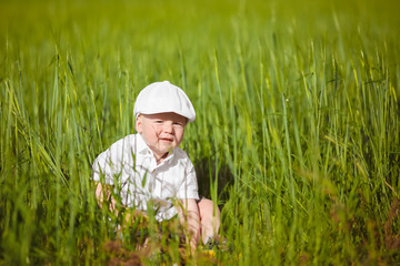 Naklejka na ściany i meble Funny little boy in white cap relax in green grass, at summer park.