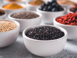 Black sesame in small white bowl and other superfoods on background. Selective focus. Different superfoods ingredients. Concept and illustration for superfood and detox food