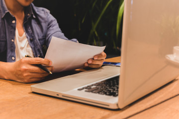 Man hand holding pen reading paper work with laptop and coffee