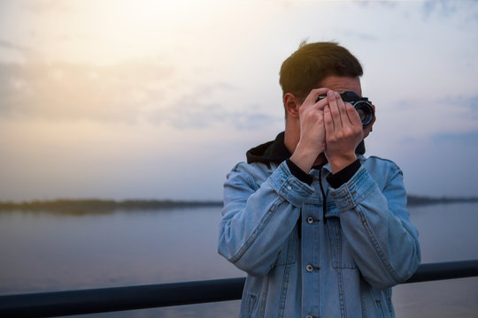 A man in a denim jacket with a vintage film camera at sunset