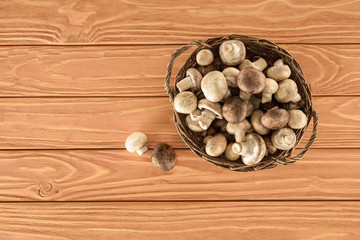 top view of raw champignon mushrooms in basket on wooden surface