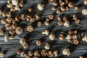 top view of uncooked champignon mushrooms spilled on wooden surface