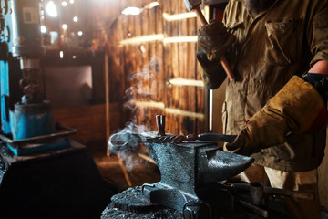Fototapeta na wymiar The blacksmith forging the molten metal on the anvil in smithy.