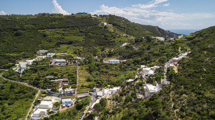 Fototapeta na wymiar Aerial view of a group of villas and small houses. These buildings are located in the green on the island of Ponza, in Italy. They are colorful houses. The sky is clear with few clouds.