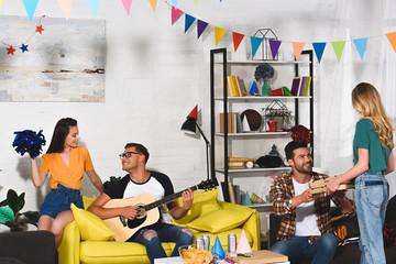 smiling young people with pizza, beer and guitar having fun together at home party