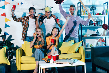 happy young male and female friends drinking beer and smiling at camera at home party