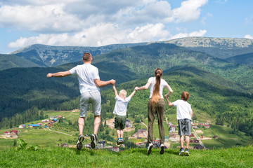 Family holiday. Parents with children jump on the background of mountains. Back view.