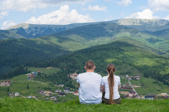 Pair of lovers sit on a hill and admire the view of the mountains. Rest together. Back view