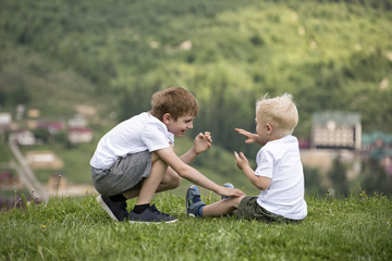 Naklejka na ściany i meble Two boys sit on a hill and have fun. Back view