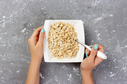 Useful And Healthy Breakfast. The Girl Took Milk To Pour It Into Oatmeal On A Gray Background, Top View