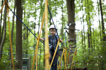Obraz na płótnie Canvas boy enjoys climbing in the ropes course adventure. smiling child engaged climbing high wire park.