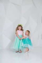 Fototapeta na wymiar Beautiful children in dresses in a white room. Girls play and laugh