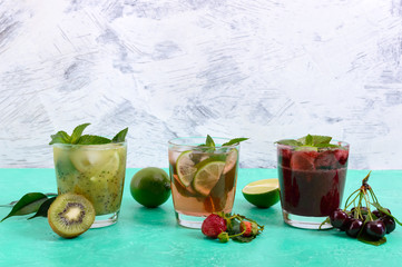 Summer cold drinks with fresh fruits, berries and mint. Strawberry mojito, cherry smoothies, cocktail of kiwi in glasses on a bright background.