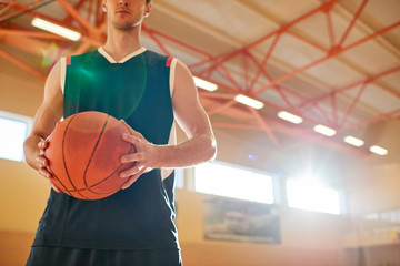 Crop man in basketball sportswear holding ball while standing on court in gym. 