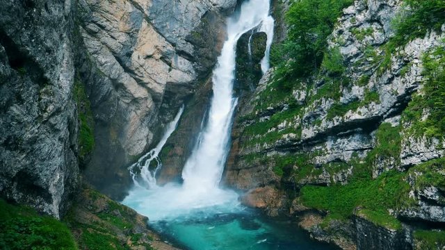 A big waterfall splashes. Waterfall is flowing down and entering the river in the canyon.