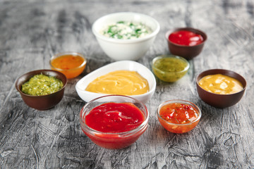 Bowls with different sauces on grey textured background