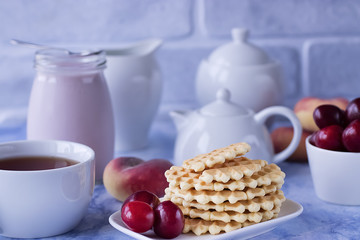 Breakfast. White cup of tea with thin waffles, lemon jam, yogurt and fresh fruit.