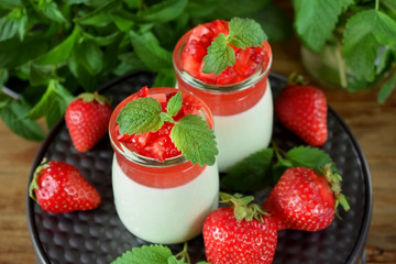 Two layered panna cotta with matcha tea topped with strawberry jelly, berries and mint in glass jars