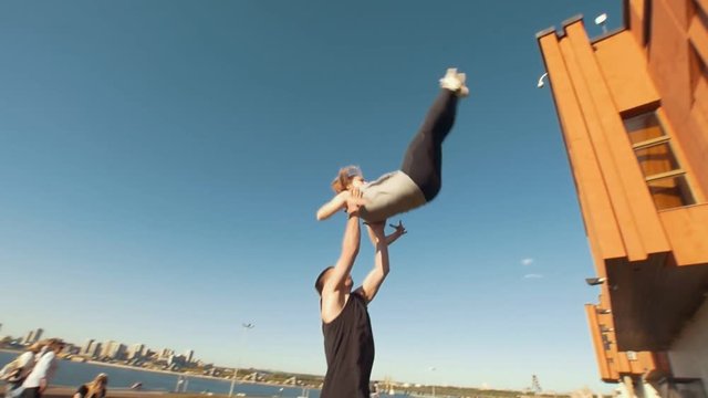 Young cheerleaders workout outdoors at cityscape on background - young man holding the girl performing flip in the air