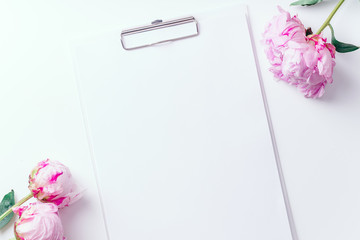 Feminine workspace with empty paper and pink peons on white background with copy space
