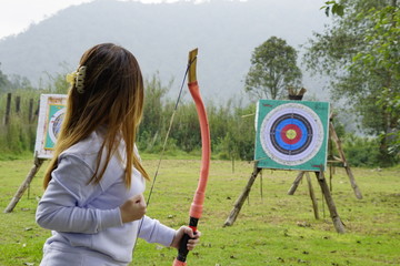 Young woman is aiming in archery  practice n the field with a target in front of her.