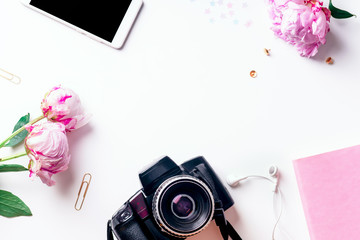 Feminine workspace with pink peons, camera and phone on white background with copy space