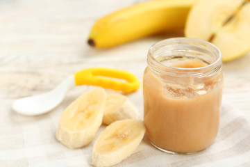 Jar with healthy baby food and cut banana on table