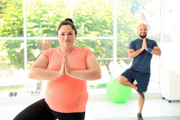 Overweight man and woman practicing yoga in gym