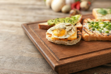 Different delicious toasts on wooden board, closeup