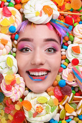 Face of beautiful young woman with creative makeup surrounded by different sweets