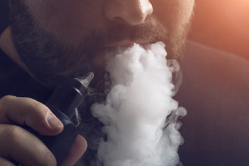 Man vape e-cigarette with e-liquid, close-up, breathes out large cloud of steam or vapor. Vaping...