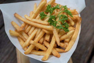 Tasty  french fries are laid on paper. A little parsley is placed on top. All were placed on wooden table background.