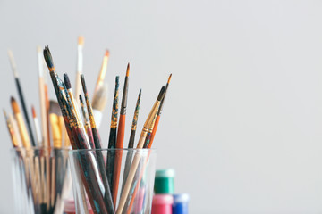 Glass with painting brushes on light background