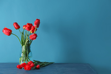 Vase with beautiful tulips on table against color background